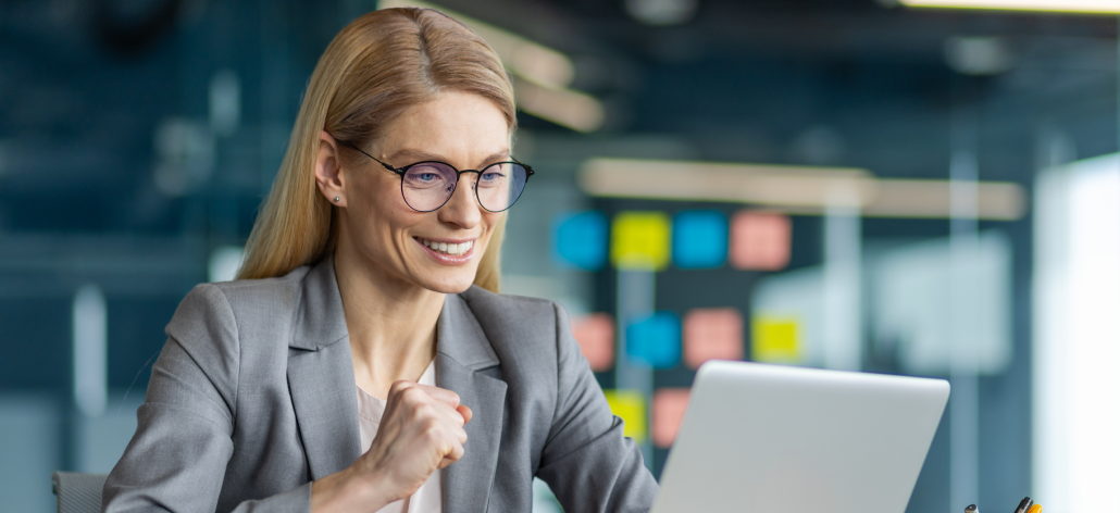 Business woman in grey suit and glasses smiles at her laptop