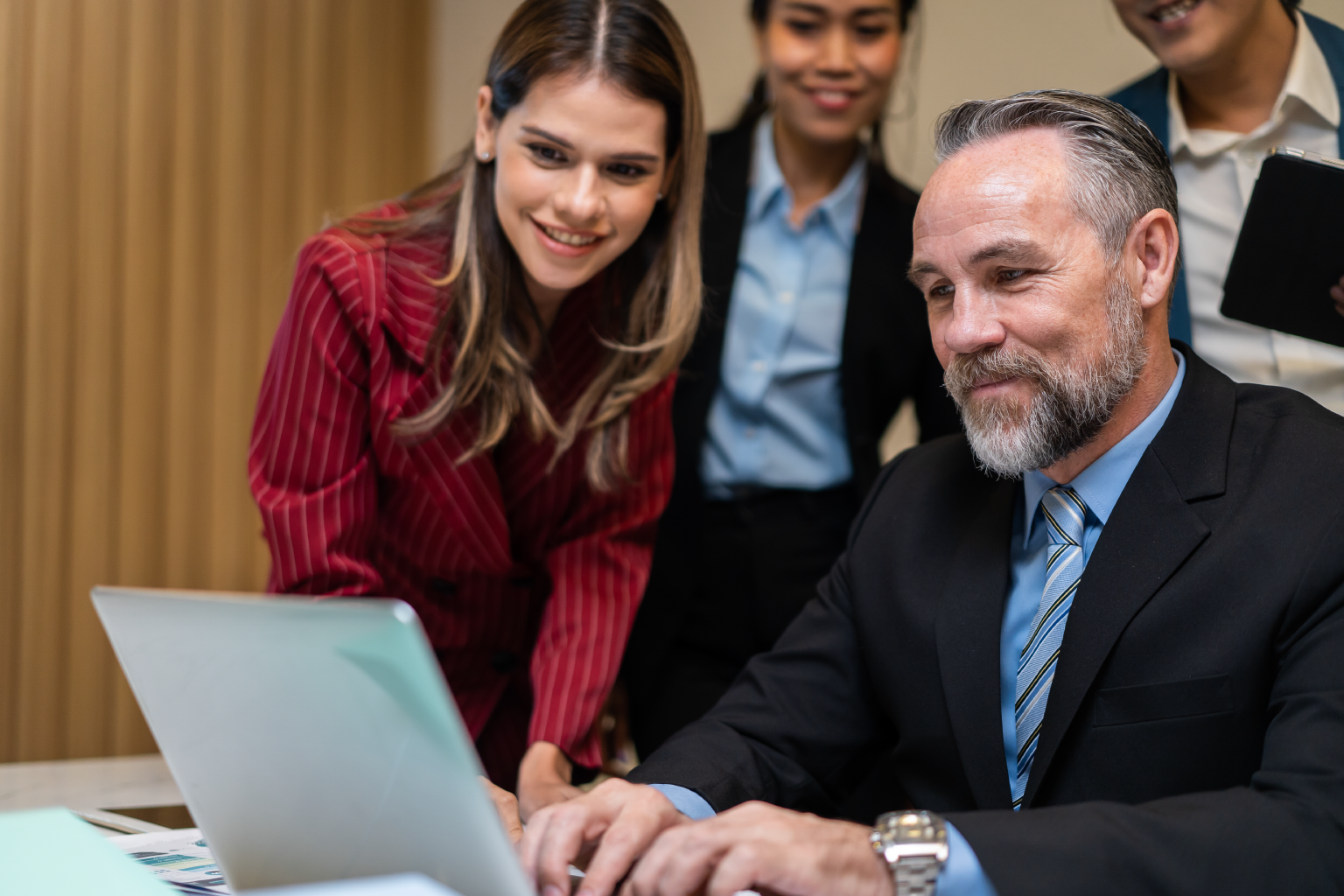 Four business professionals smile at a laptop.