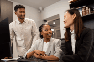 Three business professionals smiling in front of a computer.