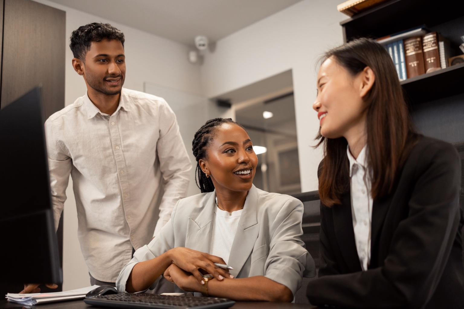 Three business professionals smiling in front of a computer.