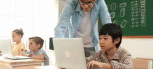 Grade school teacher helps student on laptop