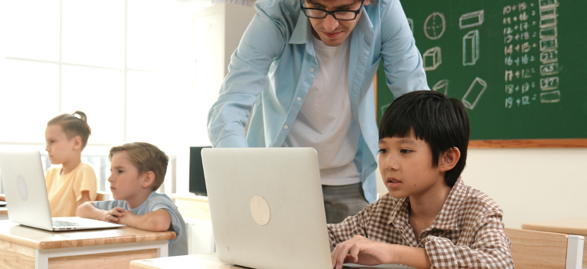 Grade school teacher helps student on laptop
