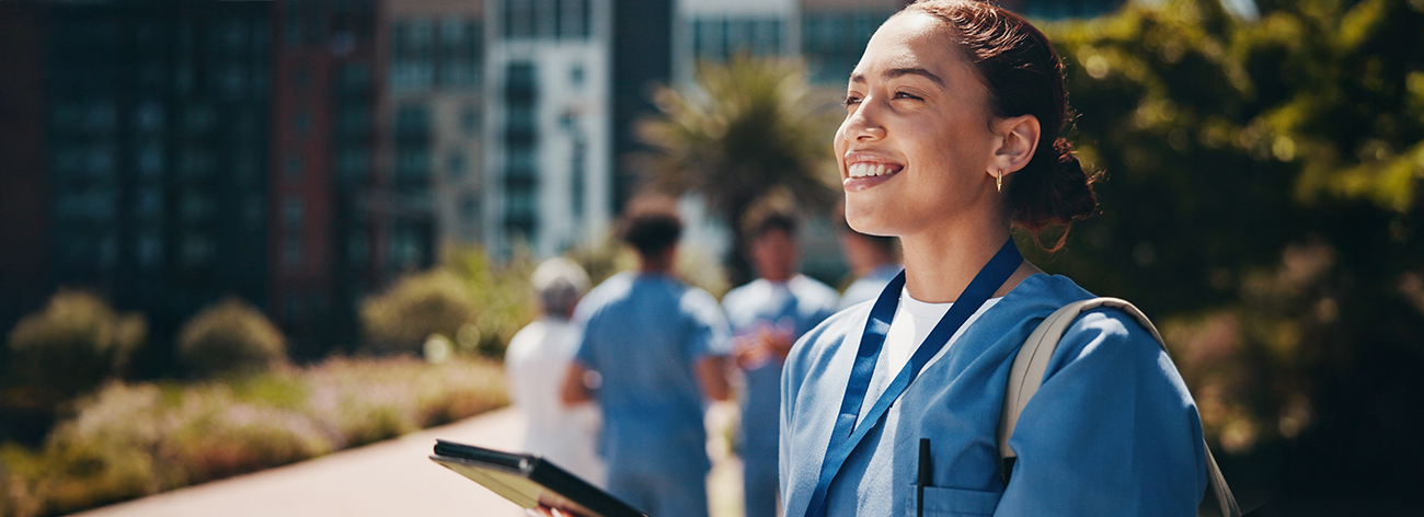 A healthcare student stands outside smiling and holding a tablet