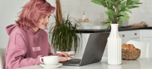 Young professional with pink hair using a laptop at home.