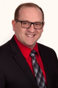 Youngstown State MBA graduate Ricky Neal wearing a black suit and red shirt in a professional photo
